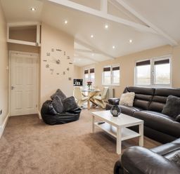 A living room with black leather sofas a white coffee table a bean bag a dining table and wall clock at Sparrows Den Lodge in Winchelsea Beach
