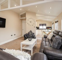 A living room with black leather sofas a white coffee table a wall clock and a wall mounted tv at Sparrows Den Lodge in Winchelsea Beach