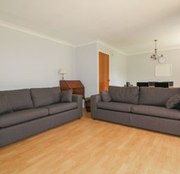 A living room with two gray sofas a wooden floor a wooden door a small wooden desk with a lamp and a dining area at Three Jays in Lanreath