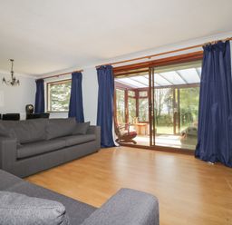 A living room with dark sofas wooden dining table and blue curtains at Three Jays in Lanreath
