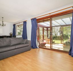 A living room with a gray couch wooden floor and dark blue curtains beside large sliding glass doors at Three Jays in Lanreath