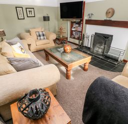 A living room with beige sofas a wooden coffee table a fireplace and a wall mounted television at Mountain Farm in Broad Haven