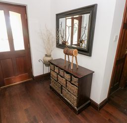 A hallway with a wooden door a wicker basket cabinet a decorative wooden reindeer a large mirror and a vase with dried plants at Mountain Farm in Broad Haven