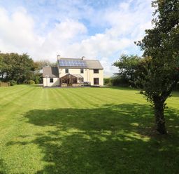 A large house with solar panels on the roof and a conservatory surrounded by a mowed lawn and trees at Mountain Farm in Broad Haven