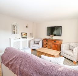 A living room with armchairs a wooden coffee table a television on a wooden cabinet and a staircase at Foundry Cottage in Reedham
