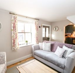 A living room with a grey sofa and patterned armchair near a window and door at Foundry Cottage in Reedham