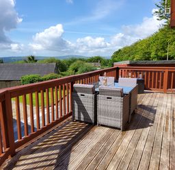 An outdoor wooden deck with a dining table and chairs overlooking greenery and hills at Lodge 11 in Tavistock