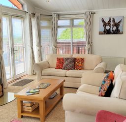 A living room with two beige sofas a wooden coffee table a wood burner and large windows at Lodge 11 in Tavistock
