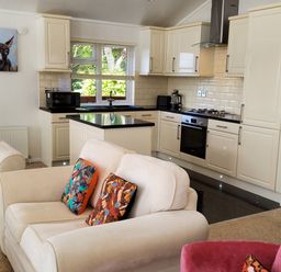 A kitchen with cream cabinets and black countertops next to a living area with beige sofas and colorful cushions at Lodge 11 in Tavistock