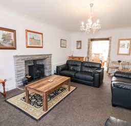 A living room with black leather sofas a wooden coffee table a stone fireplace and a dining area at Halcyon Moelfre near Benllech