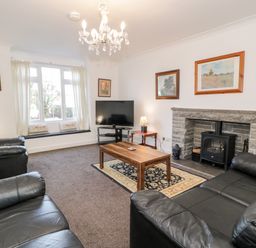 A living room with black leather sofas a wooden coffee table a stone fireplace and a television at Halcyon in Moelfre near Benllech