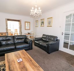 A living room with two black leather sofas a wooden coffee table and a dining area at Halcyon in Moelfre near Benllech