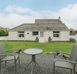 A small outdoor seating area with two chairs and a round table in front of a single-story house at Halcyon Annexe Moelfre near Benllech