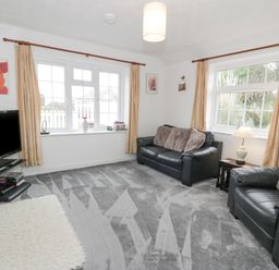 A living room with two black leather sofas cushions a television on a stand and windows with curtains at Halcyon Annexe in Moelfre near Benllech