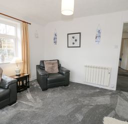 A living room with black leather sofas a side table with lamp and decorative items on a grey carpet at Halcyon Annexe in Moelfre near Benllech