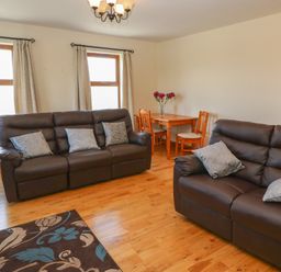 A living room with two brown sofas and cushions a wooden dining table with chairs and vase of flowers at Dooneen near Castletownshend County Cork