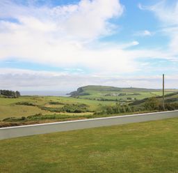 A grassy lawn with a low wall overlooking green fields hills and a partly cloudy sky at Dooneen near Castletownshend County Cork