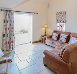 A sitting room with two leather sofas a wooden chair with cushion and a lamp at Bryn Eiddon in Aberdaron