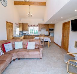 A kitchen and living room with a brown leather corner sofa and a grey armchair at Bryn Eiddon in Aberdaron