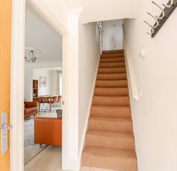 A carpeted staircase next to an open door leading to a room with brown chairs and a dining table at 5 Styleman Road Hunstanton