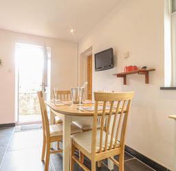 A dining area with a wooden table and chairs a wall-mounted TV and a door leading outside at Y Bwthyn Newport in Newport Pembrokeshire