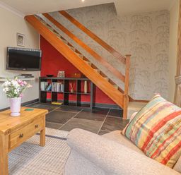 A living room with a wooden coffee table flowers on the table a sofa with a striped cushion television on the wall and wooden stairs at Y Bwthyn Newport