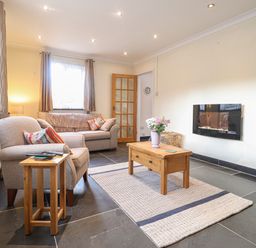 A living room with two armchairs a coffee table and a wall-mounted electric fireplace at Y Bwthyn Newport
