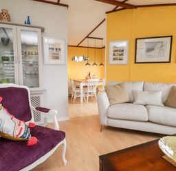 A living room with a beige sofa and purple armchair next to a glass cabinet and a dining area visible beyond at 4 Country View Park in Graveney near Seasalter