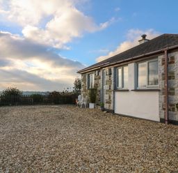 A stone and brick house with gravel ground and a small white table and chairs outside at Valley View in Mevagissey