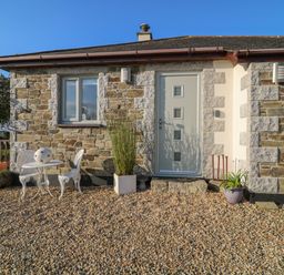A stone cottage exterior with a gray door and windows a small white table and chairs and potted plants at Valley View in Mevagissey