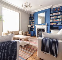 A living room with beige sofas striped blankets a wooden coffee table a chandelier and blue built in bookshelves at The Water House in Falmouth