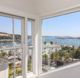 A view through corner windows showing houses, a harbor with many boats, and hills in the background at The Water House in Falmouth