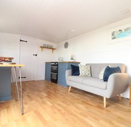A kitchen and sitting area with a grey sofa and blue cabinets at Sebright in St Austell