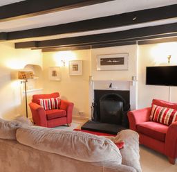A living room with two red armchairs a beige sofa a fireplace and a wall mounted television at Milkwood Cottage in Fishguard Pembrokeshire