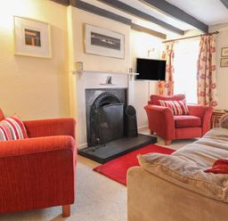 A living room with red armchairs a beige sofa a fireplace and a wall-mounted TV at Milkwood Cottage in Fishguard Pembrokeshire