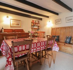 A dining room with a wooden table covered by a red and white tablecloth surrounded by wooden chairs and bench at Milkwood Cottage in Fishguard Pembrokeshire
