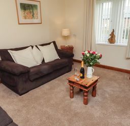 A living room with a sofa, coffee table, flowers, and a TV at The Retreat in Embleton