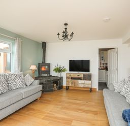 A living room with two sofas a wood burning stove and a television on a cabinet at Red Ridge in Llandanwg near Harlech