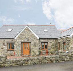 A stone house with wooden doors and windows and a slate roof behind a low stone wall at Red Ridge in Llandanwg near Harlech