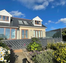 A two story house with dormer windows and glass doors with a garden and flowers in front at Red Ridge in Llandanwg near Harlech