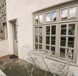 An outdoor patio area with a small round metal table and two matching chairs outside a house with a beige door and large multi-pane windows at 3 Alma Terrace in Llanfairfechan