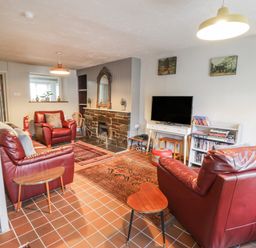 A living room with red leather sofas a television and a fireplace at 3 Alma Terrace in Llanfairfechan