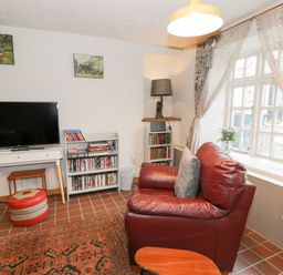 A sitting room with a red leather chair television and bookshelf near a window at 3 Alma Terrace in Llanfairfechan