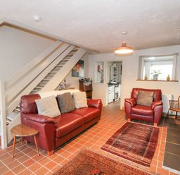 A living room with red leather sofa and armchair with cushions and a small wooden side table at 3 Alma Terrace in Llanfairfechan