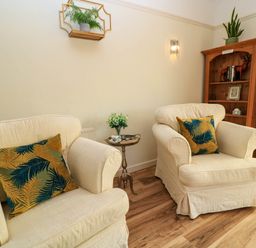 A sitting area with two cream armchairs and patterned cushions a wooden shelf and a small side table with flowers at Downs View in Norton Ferris