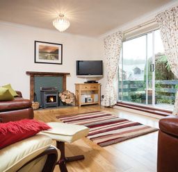 A living room with a fireplace a television a striped rug and sliding glass doors at Nutwood in Lakeside