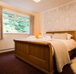 A bedroom with a wooden bed frame bedside tables and patterned curtains at Nutwood in Lakeside