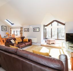 A living room with leather sofas cushions a wooden dining table and large windows at Spring Cottage in Ambleside