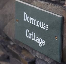 A close up of a green sign with white text mounted on a stone wall at Dormouse Cottage in Coniston