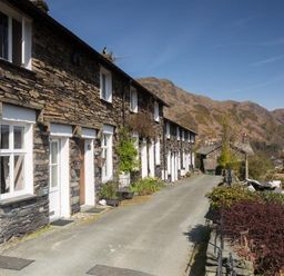 A row of stone cottages with white doors and windows along a narrow road with hills in the background at Dormouse Cottage in Coniston